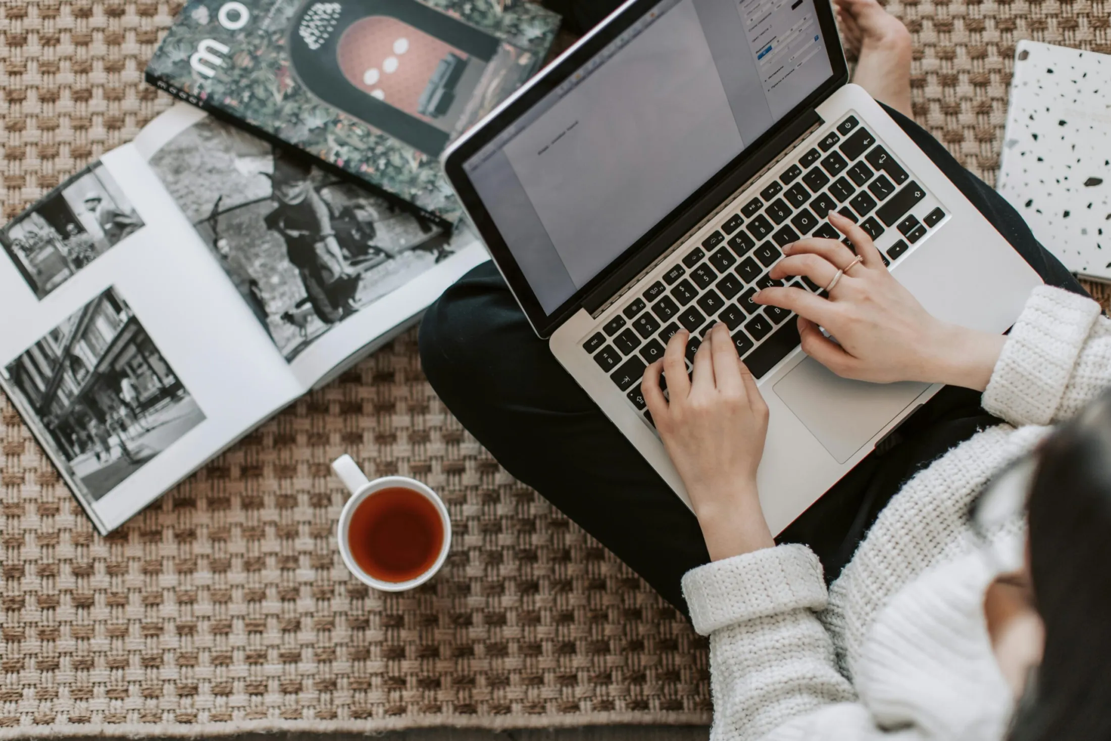 Content writer drafting website copy on a laptop beside a cup of tea and open magazines